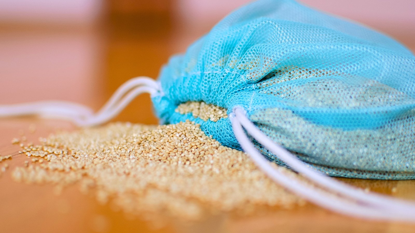 Μικροί, στρογγυλοί, λευκοί σπόροι quinoa σε μια καθαρή μπλε επαναχρησιμοποιήσιμη τσάντα σε ένα ξύλινο τραπέζι.