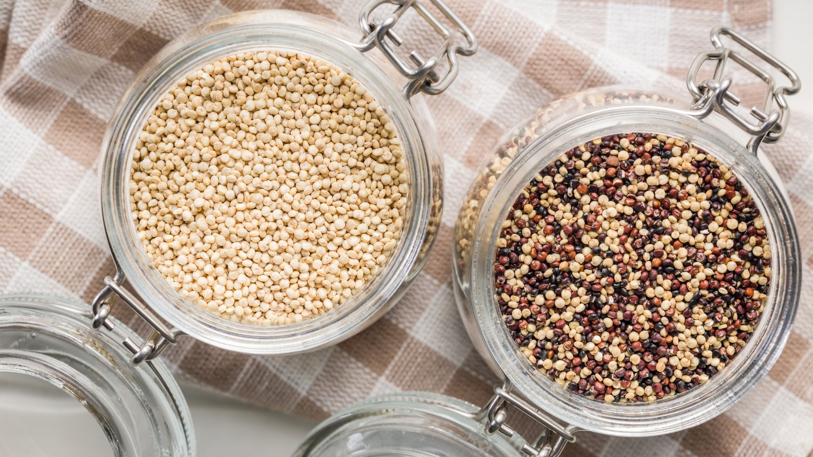 Κάτω από πολύχρωμες σπόρους quinoa σε δύο γυάλινα βάζα με καπάκια που στέκονται σε μια καρώτσιμη χαρτοπετσέτα.