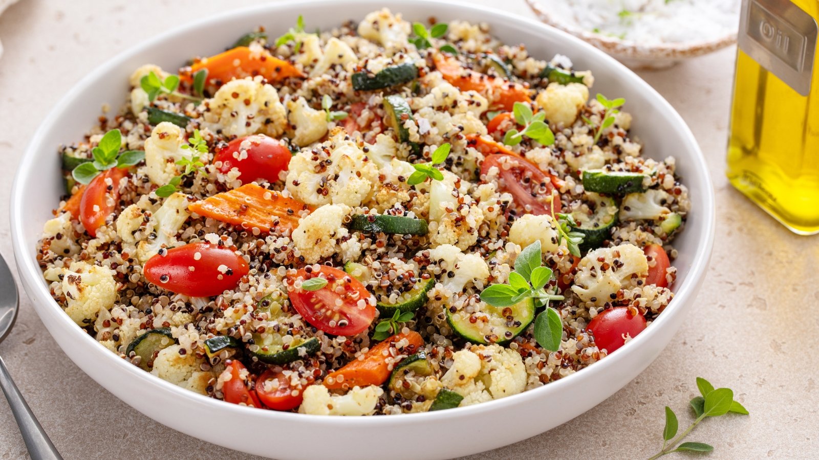 Κλείστε τη σαλάτα quinoa με ψητά λαχανικά, κουνουπίδι και κολοκυθάκια, και φρέσκα βότανα και ντομάτες σε μια μεγάλη λευκή πλάκα.